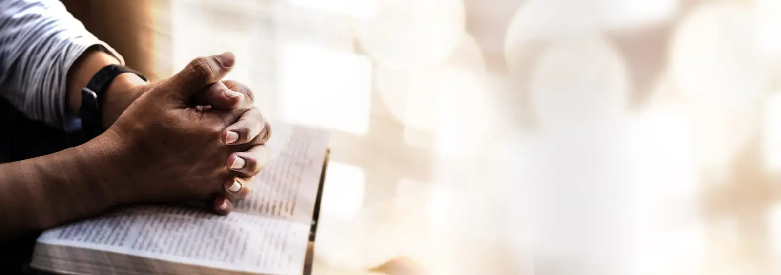 Hands folded in prayer over an open Bible