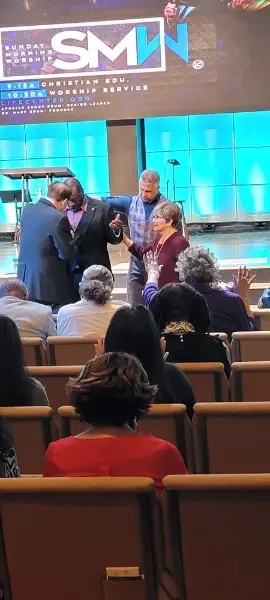 Two men on the platform edge praying with a woman during Sunday morning worship
