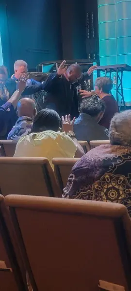 The speaker with arms raised, the congregation praying in the rows in front