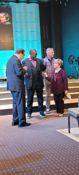 Three men and a woman standing together on the platform, one holding a microphone