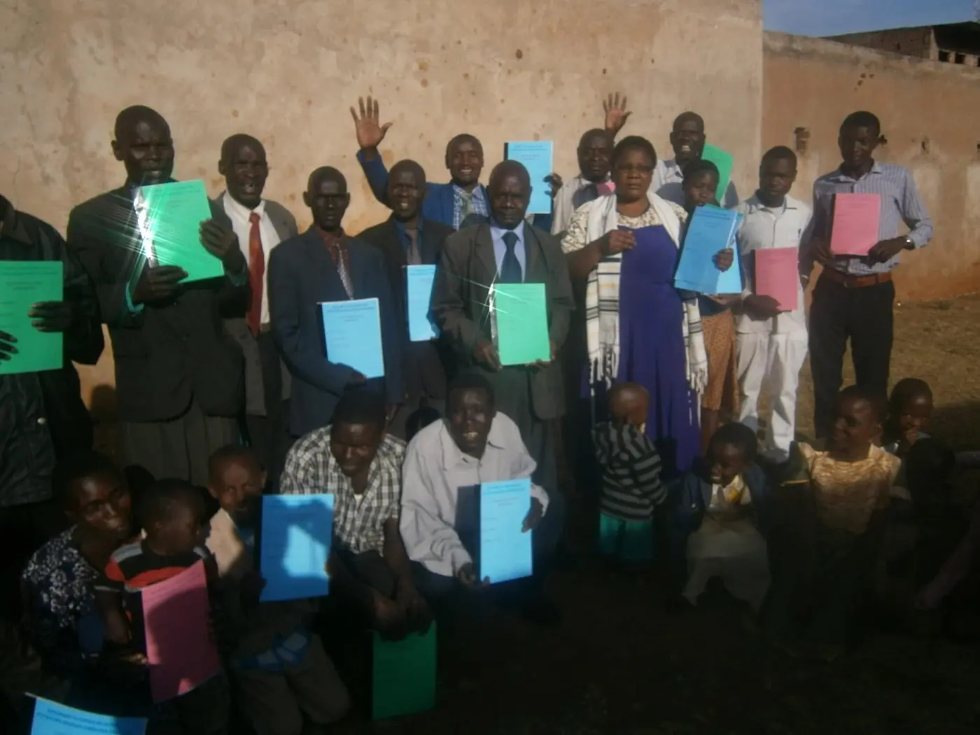 A Kenyan gathering standing against a compound wall, each person holding a Bridge Builders manual