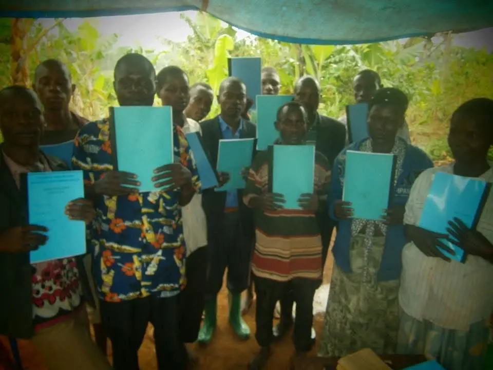 A group under a tarpaulin, each person holding a blue Bridge Builders manual