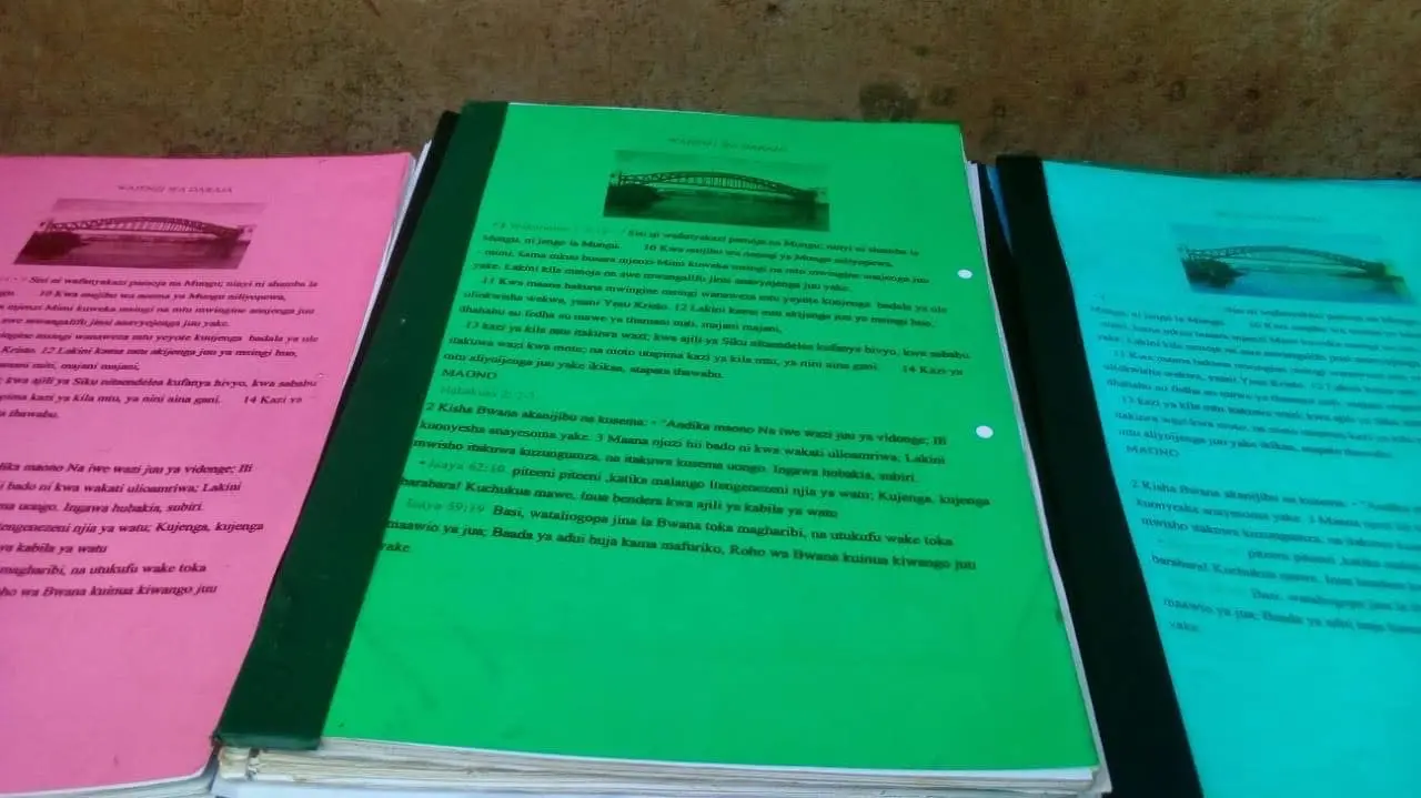Hand-bound Wajenzi wa Daraja training manuals, each cover carrying a photograph of a bridge